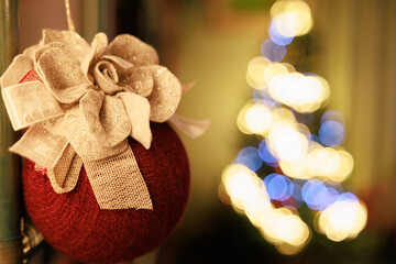 sfera rossa con una decorazione di stoffa legati a forma di rosa, in primo piano, albero di natale con luci colorate su sfondo sfuocato © PhotoMet