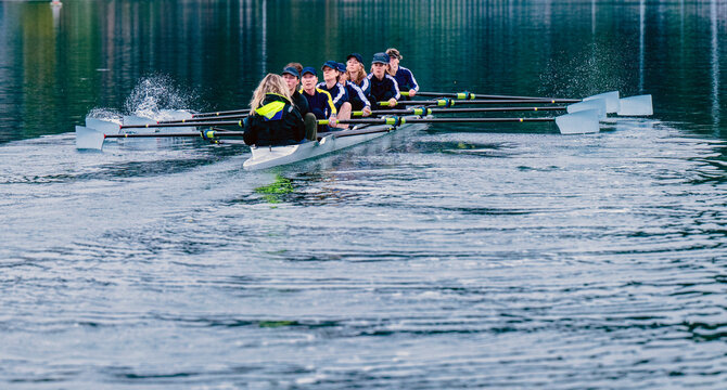 An eight-white person rowing team rows together in calm water