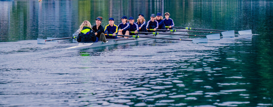 A white women's rowing team practices together on a calm lake