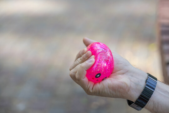 Close-up of hand squeezing pink squishy stress relief toy outdoors
