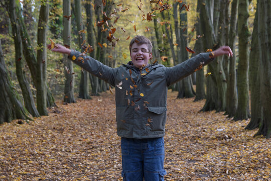 Child joyfully playing in a forest while throwing fallen leaves during autumn season
