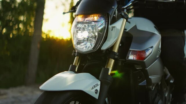 Motorcyclist in black helmet riding modern sport bike along forest road at golden sunset, front closeup and rider portrait emphasizing speed and adventure