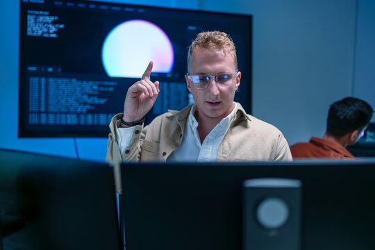 Young male software developer raising finger with an idea while working on programming code and AI system analysis on computer in modern IT office