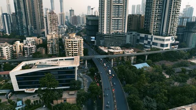Cinematic aerial drone footage showing Mumbai's dense urban landscape, with modern high-rise buildings, older residential structures, an elevated metro line, busy roads and ongoing construction.