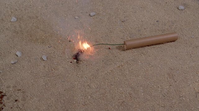 A dynamite cartridge about to explode falls on a sand terrain.