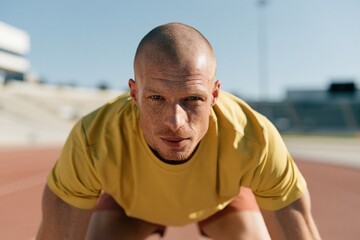 Fototapeta premium Focused male sprinter in starting position on outdoor track for athletic poster background and training banner design