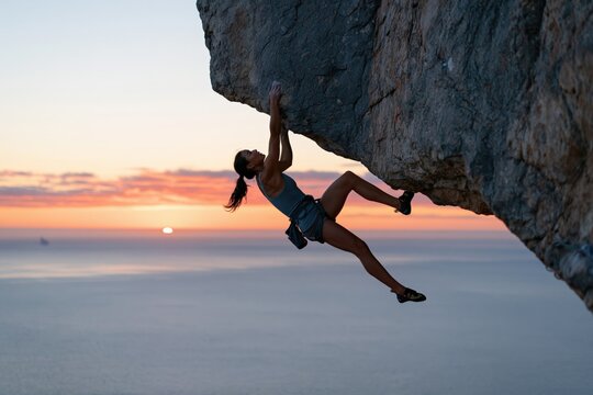 Woman overhanging rock climber on coastal cliff at sunset background for adventure poster and outdoor sport design