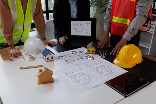 Construction professionals discussing building plans and property designs, using a laptop and schematics for urban development