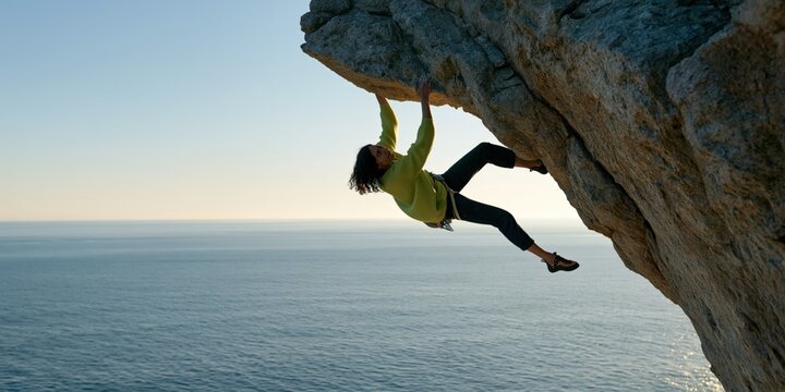 Rock climber hanging from a coastal cliff over the sea at sunset for adventure poster and outdoor sports background
