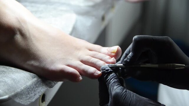 Pedicurist gently pushes back the cuticle on a woman's toenails using a metal cuticle pusher. Close-up professional pedicure and nail preparation procedure.