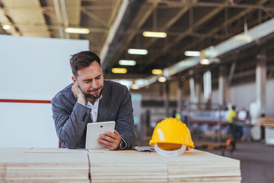 Business Manager In Factory Reviewing Tablet During Inspection With Yellow Hard Hat On Workbench