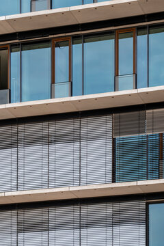Horizontal blinds divide a building into layered bands, while windows and glass trace clean lines across the facade, turning modern urban architecture into a close detail.