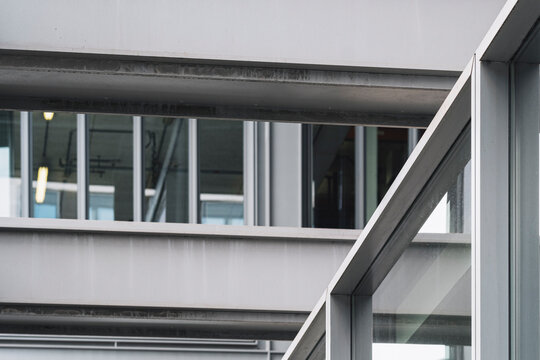 A corridor crosses the frame beneath horizontal structure, while glass windows and clean lines reveal a facade detail within modern urban architecture.
