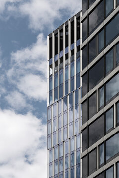 Clouds drift beside a tower as reflections move across its facade, while modern office windows and glass draw vertical lines through urban architecture against the sky.