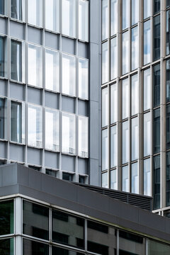 A layered building catches light across its facade, where reflection moves over glass windows and modern office geometry within the surrounding urban architecture.