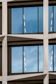 Sky reflection settles into broad windows framed by concrete, while the facade reveals a precise detail of modern office geometry within the surrounding urban architecture.