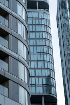 A narrow perspective looks between towers as reflective surfaces rise, while curved windows and glass form vertical bands and the facade compresses modern urban architecture.