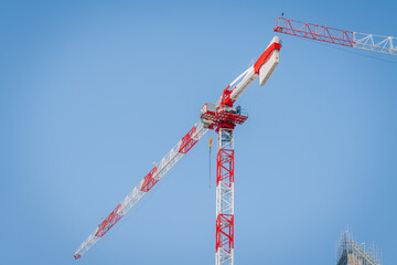 Construction crane with red and white color scheme against a clear blue sky, part of a building site in Milan, Italy © Raivo