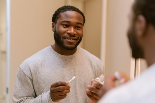 Man smiles while brushing teeth in bathroom mirror