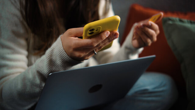 Anonymous young woman shopping online from home with her payment card, focused on completing a digital purchase.