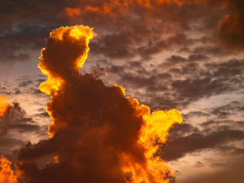 Striking cloudscape at sunset in summer, with dark, anthropomorphic figure like a mythical giant on fire and in motion. Motifs of pareidolia, fight-or-flight response, legend.