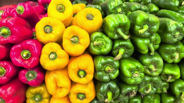 Panning shot over a vibrant display of fresh red, yellow, and green bell peppers neatly stacked at a market. Great for healthy food concepts.