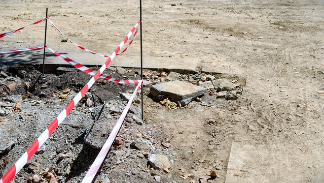 Construction site featuring red and white barrier tape marking a dangerous excavation zone, indicating active road work and public safety precautions during urban development projects