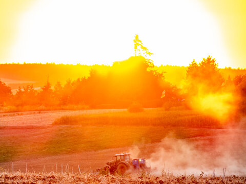 Traktor wirbelt Staub auf bei Sonnenuntergang