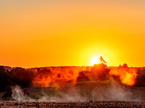 Traktor wirbelt Staub auf bei Sonnenuntergang