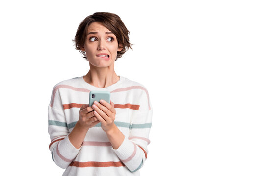 Photo of guilty sad young woman dressed striped pullover holding modern device looking empty space isolated grey color background