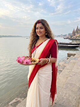 Indian woman in traditional saree holding lotus flowers by the ganges river