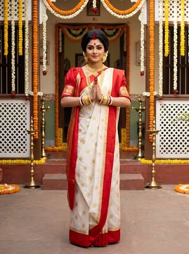 Beautiful bengali bride in traditional white and red saree greeting with namaste