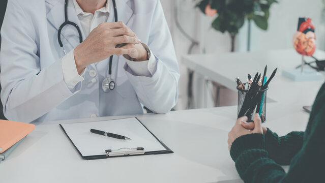 A male doctor is listening to and counseling an Asian female patient at his desk in a clinic during a health check-up.