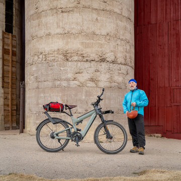 senior male cyclist with a touring electric bike is taking a rest break at old barn in rural Colorado