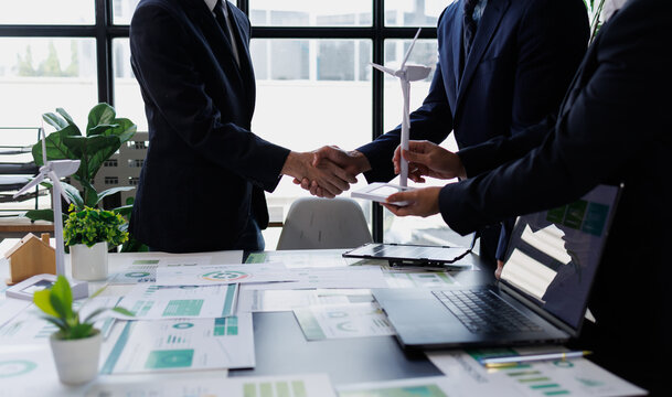 Business partners shaking hands, collaborating on renewable energy project, discussing sustainable green technology development