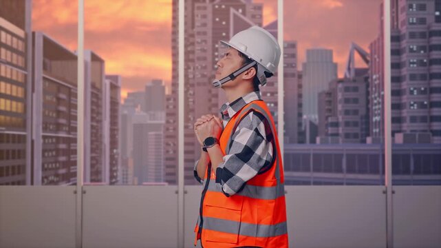 Side View Of Asian Male Engineer With Safety Helmet Pray For Something While Standing at Office with Panoramic City Skyline at Sunset