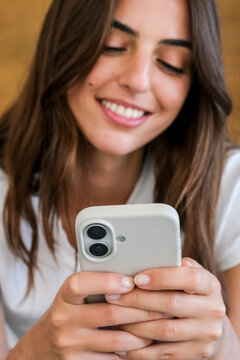 Smiling young woman looking at smartphone while texting, relaxed and happy, close-up of hands and mobile device showing everyday technology, communication and social media use