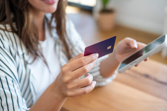 Woman holding credit card and smartphone while making online payment at home, smiling during mobile shopping and contactless transaction for e-commerce, finance and digital banking