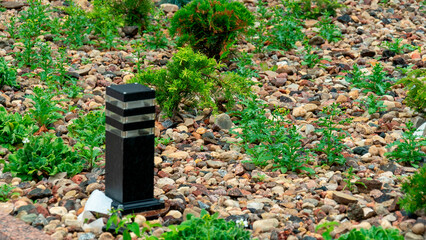 Square stone marker stands among pebbles and plants in a garden setting near a walking path during the day © Сергей Семенов
