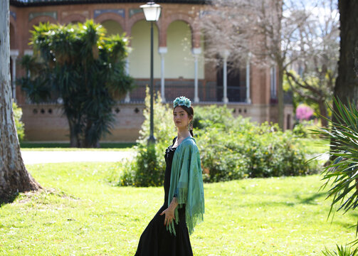 Portrait of a beautiful woman dancing flamenco whilst strolling through a park in Seville. She is wearing a black ruffled dress and a turquoise shawl. Flamenco, a UNESCO Intangible Cultural Heritage.
