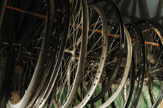 Multiple bicycle wheels are stored inside a professional bike repair workshop. Rims, tires and spoked wheels hang on a wall rack for service and replacement