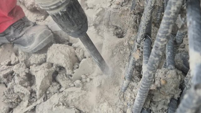 High angle close up of demolition hammer breaking concrete wall with sparks and flying debris showing the internal steel armature.