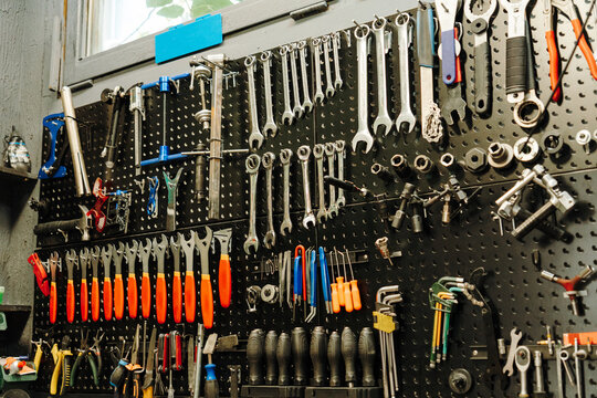 Large collection of bicycle repair tools is organized on a workshop pegboard. Wrenches and specialized equipment show a professional bike maintenance workspace