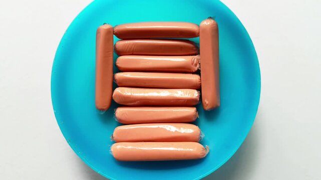 Raw packaged frankfurter sausages arranged on blue plastic plate isolated on white background