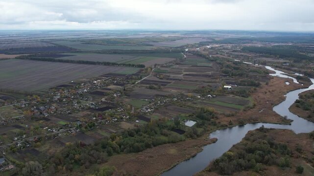 Aerial drone view of the winding Ros river flowing through agricultural fields, reeds, and a rural village in Ukraine.