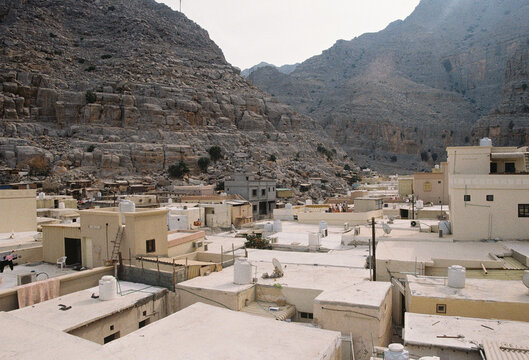 Flat-roofed village buildings nestled below massive rocky mountains.
