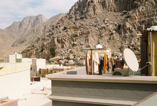 Rooftop laundry and satellite dish against a rocky mountain backdrop.