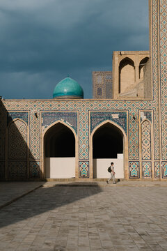 Man walking past an intricately tiled historic building in Bukhara.