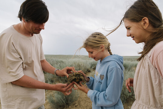 Man and two girls looking at a tortoise outdoors