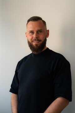 Man With a Beard Stands in Front of a White Wall Indoors